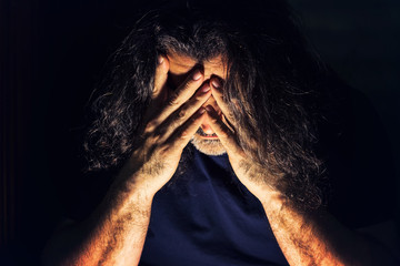 Depressed, sad man with long hair covering his face with his hands