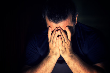 Depressed, sad man covering his face with his hands