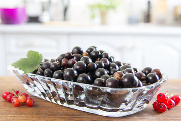 Plate of red currant on the wooden board. Top wiew, closeup. White kitchen at the background