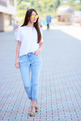 smiling beautiful woman in a jeans, walking along the light wall