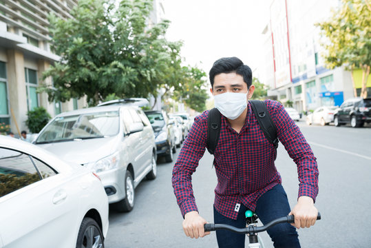 Young Guy In Face Mask Riding Bike In The Street