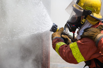 Fototapeta premium fireman in fire fighting suit spraying water to fire surround wi