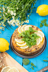 Beautiful Tasty Fresh Lemon Cheesecake with Mint on Blue Wooden Background with Chamomile Flowers, Vertical View, Close-up