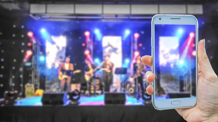 Fototapeta premium hand holding smart phone on blurred photo of music band