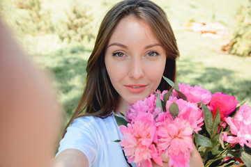 Naklejka premium Woman with flowers peonies outdoors making selfie