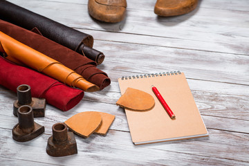 Brightly colored leather in rolls, working tools, shoe lasts, notebook with pencil on white...