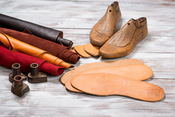Set of leather in rolls, craft tools on white wooden background. Workplace for shoemaker. Working...