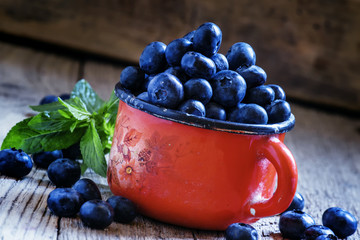 Ripe blueberries in red enamel mug, vintage wooden background, r