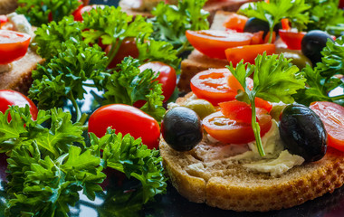 Bruschetta with green and black olives, feta cheese, cherry tomatoes, parsley and red pepper on black background. Healthy snack, breakfast, brunch.