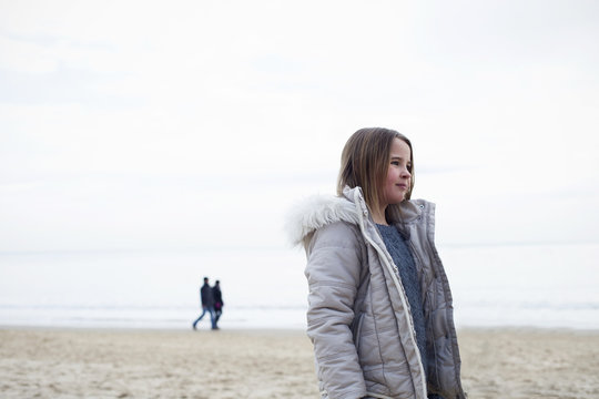 Young Girl Walking On Beach Wearing Coat