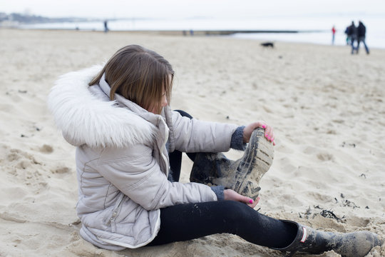 Young Girl Taking Off Wellington Boots For Walk On Beach 