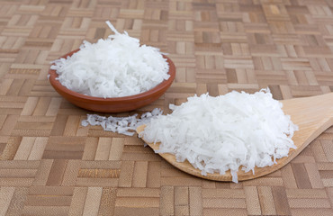 Sweetened coconut flakes on a spoon and in bowl on a cutting board.