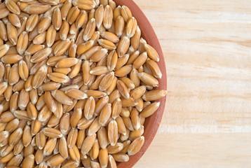 Small bowl filled with organic spelt on a wood table top view.
