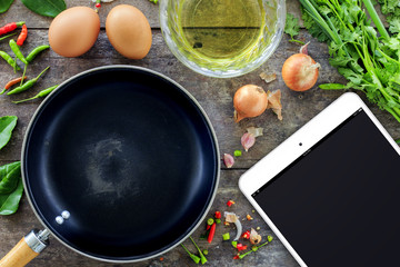 cooking concept, tablet computer and  frying pan and vegetables with eggs on wooden background, over light