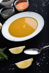 Cream soup of assorted lentil. Yellow and green lens, spices as raw for meal and lemon on black background. Healthy, appetizing, delicious, vegetarian food. Top view, copy space.