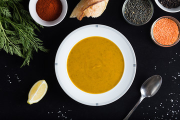 Cream soup of assorted lentil. Yellow and green lens, spices as raw for meal and lemon on black background. Healthy, appetizing, delicious, vegetarian food. Top view, copy space.