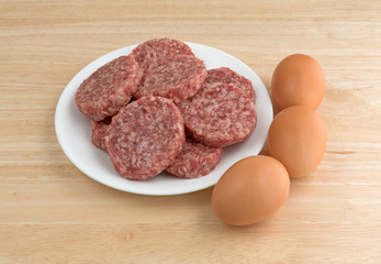 Sausage patties on a white plate with eggs to the side on a wood counter top.