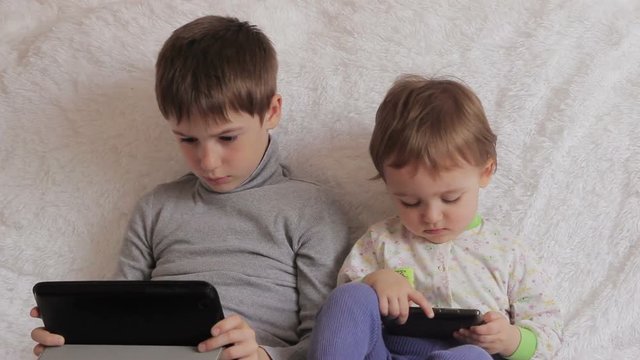 Children sitting on the couch playing on your tablet and phone to computer games