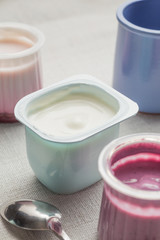 Yogurts assortment  in plastic bowls on light cloth background. Natural and fruit healthy, diet, gourmet dessert for granola breakfast. Sweet yoghurts closeup.
