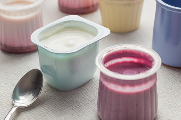 Obraz na płótnie Canvas Yogurts assortment in plastic bowls on light cloth background. Natural and fruit healthy, diet, gourmet dessert for granola breakfast. Sweet yoghurts closeup. 