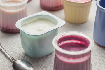 Obraz na płótnie Canvas Yogurts assortment in plastic bowls on light cloth background. Natural and fruit healthy, diet, gourmet dessert for granola breakfast. Sweet yoghurts closeup. 