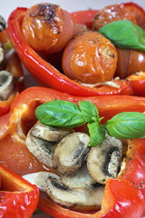 Two baked peppers with several leaves of basil, champignons and cherry