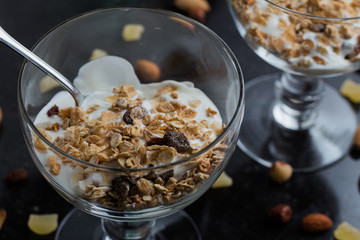 Granola with yoghurt, nuts and fruits in glass bowl on dark background. Delicious, healthy sweet dessert for breakfast. Cereal, muesli.  Copy space, closeup.
