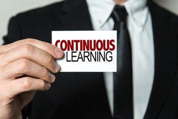 Business man holding a card with the text: Continuous Learning