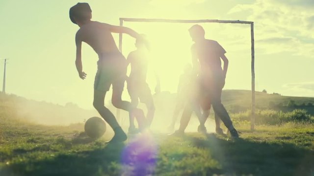 Children are playing football in the sunshine day in a village. Slow motion.