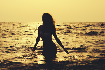 Silhouette of a slender woman in the water at the beach in sunsh