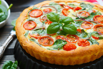 Summer outdoor tart, pie of fresh vegetables - tomatoes, spinach and red onion with cream and cheese. Selective focus
