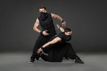 Two male dancers posing in ninja costumes on dark gray backgroun © Dmytro Panchenko