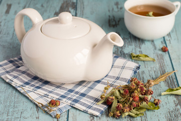  Tea. Teapot on a napkin, sprigs of the dried of wild strawberry and a cup of tea on a blue wooden background.