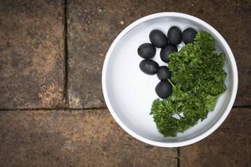 Black olive and green parsley in white bowl on brick floor background