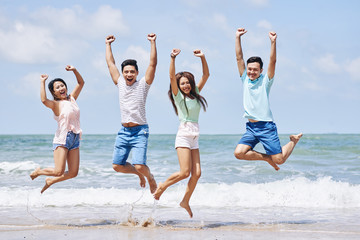 Four cheerful Vietnamese young people jumping on beach