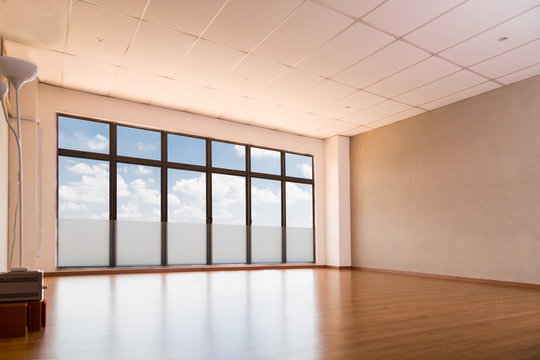 Empty yoga and dance studio with wooden flooring, windows with blue sky