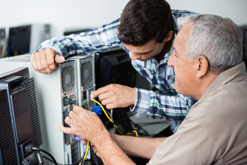 Teacher And Senior Man Fixing Computer In Class