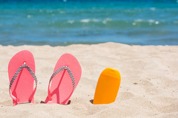 Fototapeta na wymiar Sunscreen bottle and pink flip flops on the beach