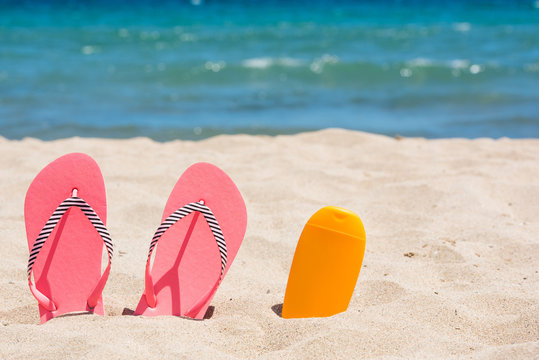 Sunscreen bottle and pink flip flops on the beach