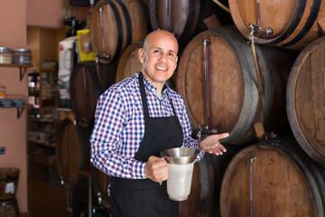 Naklejka na ściany i meble Positive man wine maker taking wine from wood