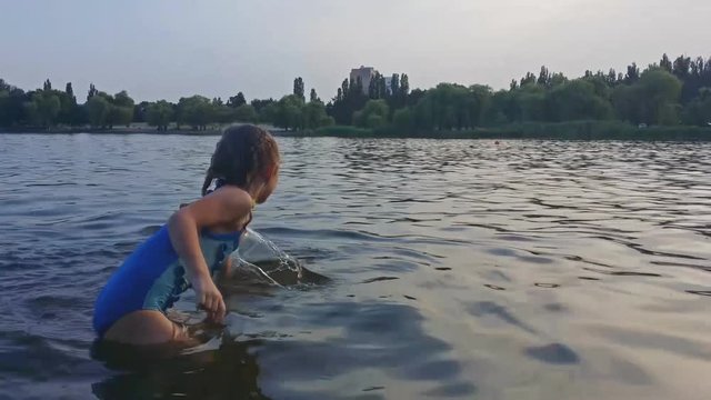 Little girl in a blue bathing suit swims away on the river