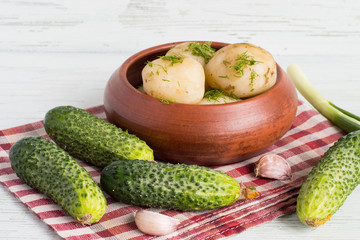  Fresh cucumbers and a bowl of boiled potatoes.   Fresh cucumbers and a bowl of boiled potatoes on a napkin on a light wooden background.