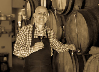 Fototapeta na wymiar Laughing male wine maker taking wine from wood