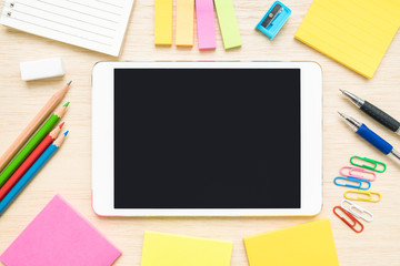 Table top view of stationery items and tablet on wooden desk