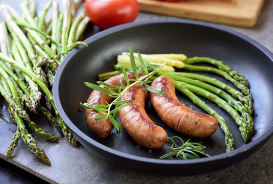 sausages with asparagus, tomatoes and rosemary on a pan