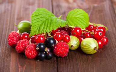 A mixture of ripe berries on a wooden table. Summer Still Life. Raspberries, gooseberries, currants close-up.