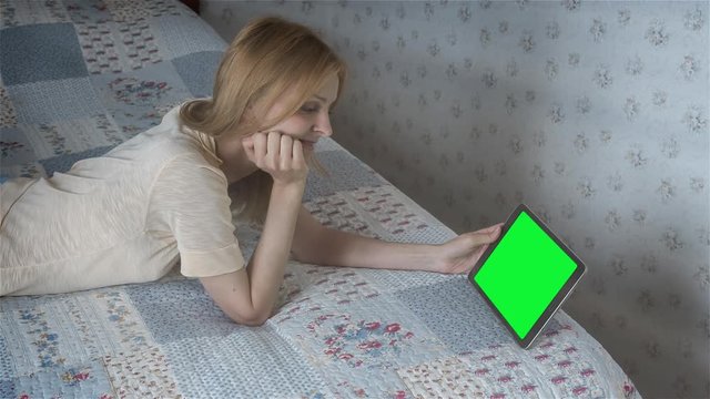 High quality 10bit footage of Beautiful girl watching movie on tablet pc with pre-keyed green screen lying on bed at home. Made from RAW footage.