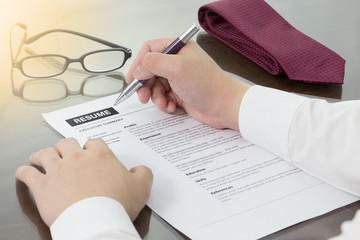 Business man review his resume on his desk or job seeker review his resume before sending to finding a new job. Resume information with pen, notebook, glasses and digital tablet.