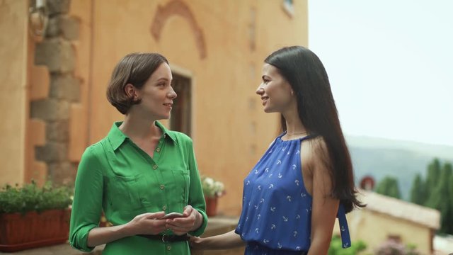 Two Attractive Young Women in Light Summer Dresses Have Conversation on Streets of European Town.