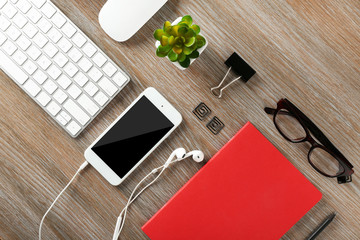 Keyboard, phone, notebook on a wooden desk background, top view